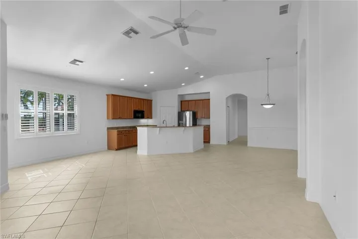 Kitchen with open floor plan, brown cabinets, a kitchen breakfast bar, arched walkways, and a center island with sink.