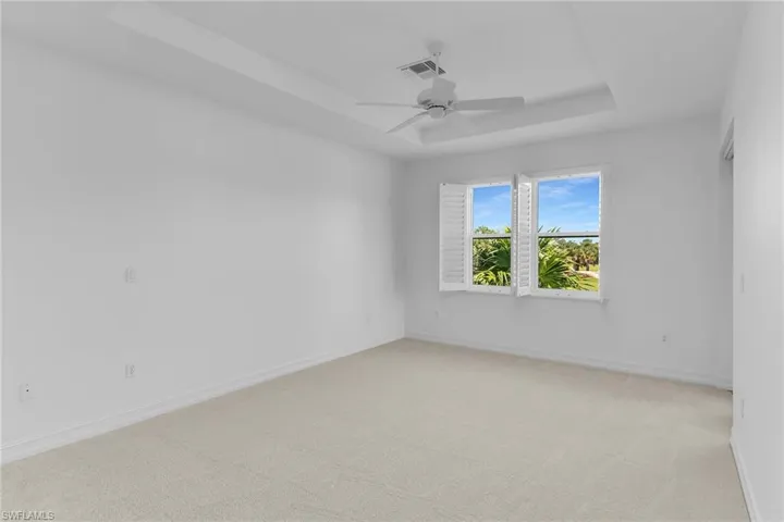 Primary bedroom featuring a raised ceiling, light colored carpet, and ceiling fan.