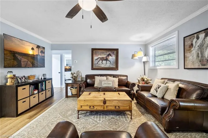 Living room with crown molding, light wood-style floors, a textured ceiling, and ceiling fan