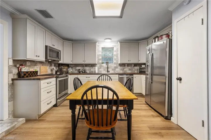 Kitchen with appliances with stainless steel finishes, light wood-style floors, tasteful backsplash, and butcher block countertops