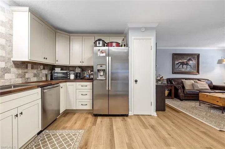 Kitchen featuring stainless steel appliances, light wood-type flooring, decorative backsplash, open floor plan, and butcher block counters