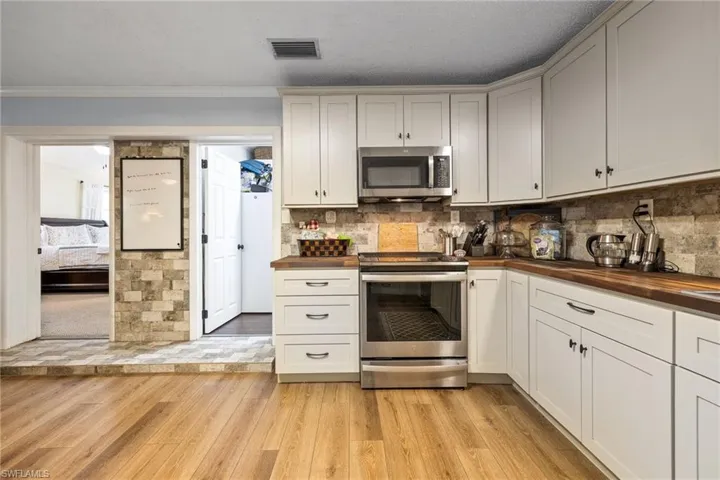 Kitchen with stainless steel appliances, wooden counters, light wood-type flooring, ornamental molding, and white cabinetry