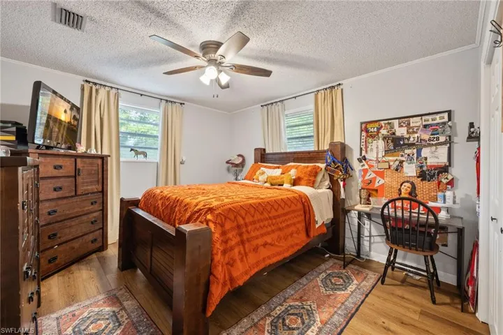 Bedroom featuring crown molding, light wood finished floors, a textured ceiling, and a ceiling fan