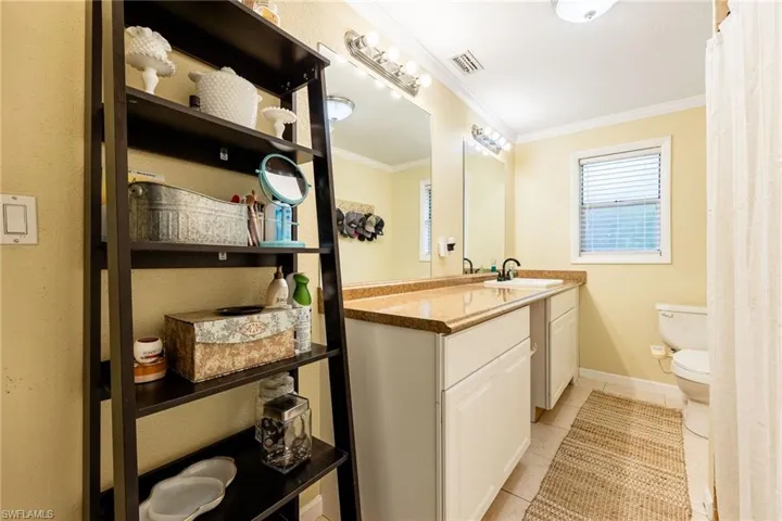 Full bath featuring light tile patterned floors, vanity, and ornamental molding