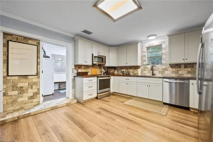Kitchen with dark countertops, crown molding, stainless steel appliances, light wood finished floors, and white cabinets
