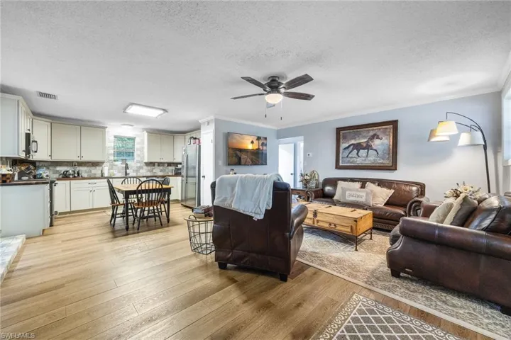 Living room featuring a textured ceiling, light wood-style floors, ornamental molding, and ceiling fan