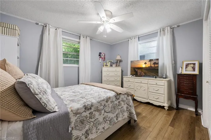 Bedroom featuring ornamental molding, dark wood finished floors, a textured ceiling, and ceiling fan