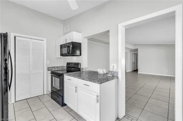 Kitchen with dark stone counters, light tile patterned flooring, white cabinets, black appliances, and crown molding