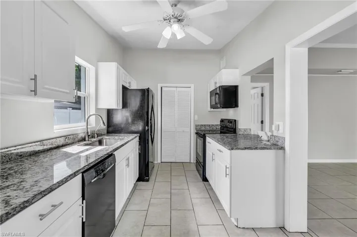 Kitchen featuring dark stone countertops, white cabinetry, black appliances, ceiling fan, and sink