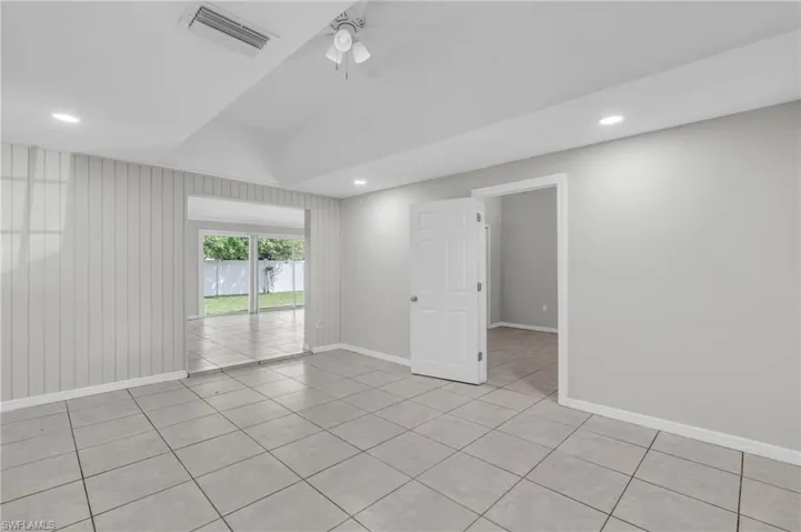 Tiled spare room featuring wooden walls, lofted ceiling, and ceiling fan