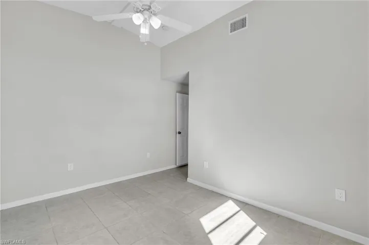 Tiled empty room featuring ceiling fan and vaulted ceiling