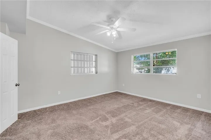 Unfurnished room featuring carpet, ceiling fan, vaulted ceiling, and crown molding
