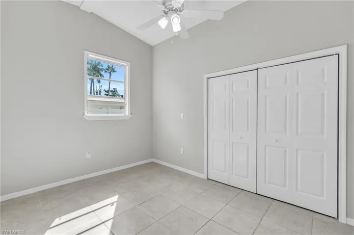 Unfurnished bedroom featuring light tile patterned floors, vaulted ceiling, ceiling fan, and a closet