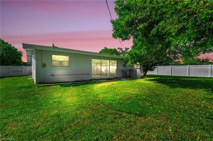 Back house at dusk with central AC unit and a lawn