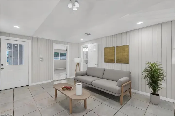 Virtually staged. Living room featuring light tile patterned flooring, wood walls, and ceiling fan