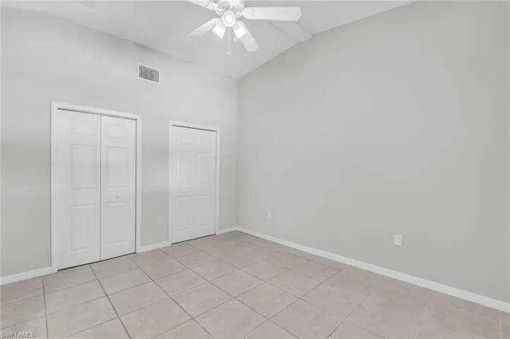 Unfurnished bedroom with high vaulted ceiling, two closets, ceiling fan, and light tile patterned floors