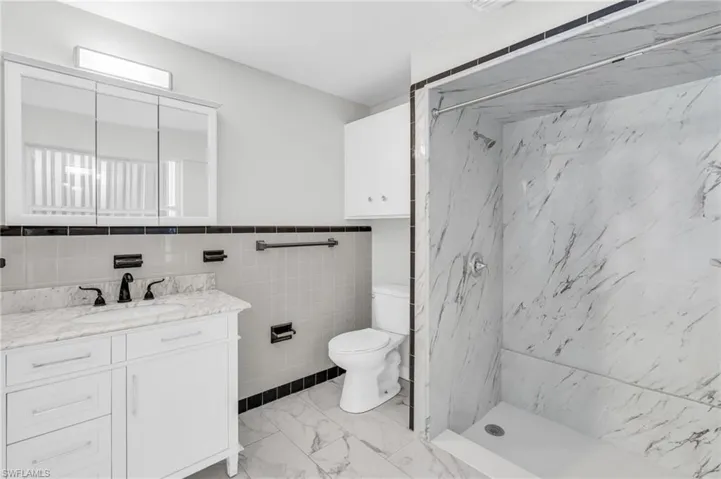 Bathroom featuring a tile shower, vanity, tile walls, and toilet