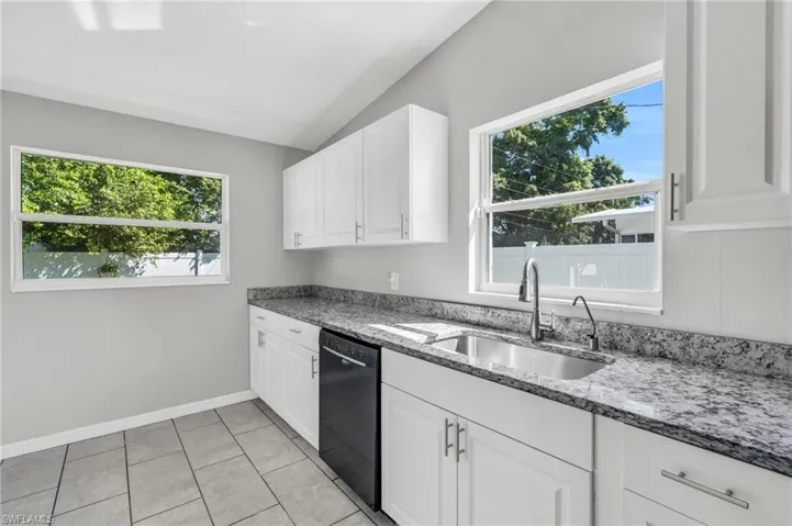 Kitchen with black dishwasher, white cabinetry, and a healthy amount of sunlight