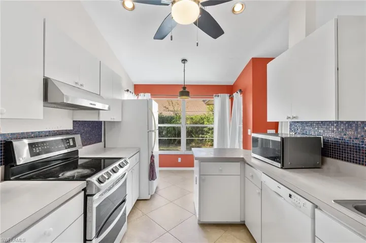 Kitchen with vaulted ceiling, backsplash, white cabinetry, appliances with stainless steel finishes, and pendant lighting