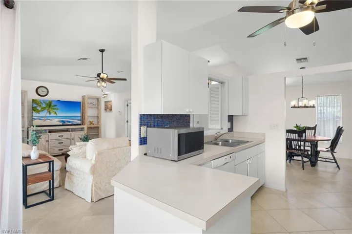Kitchen with tasteful backsplash, ceiling fan with notable chandelier, light tile floors, sink, and white cabinetry