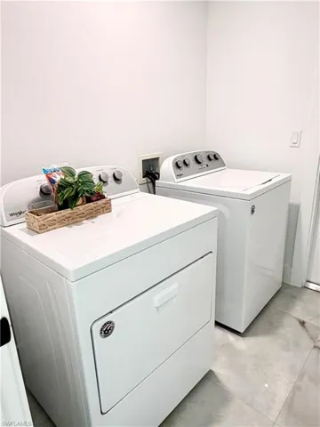 Dedicated laundry area featuring white walls, light-toned tiled flooring, and electrical outlets