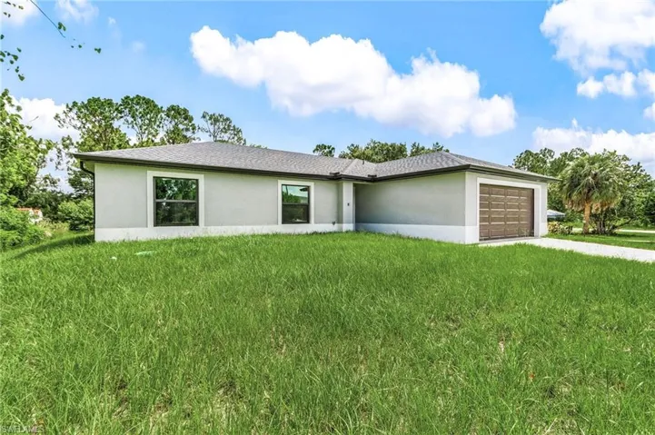 View of front facade featuring stucco siding, a garage, a front yard, and concrete driveway