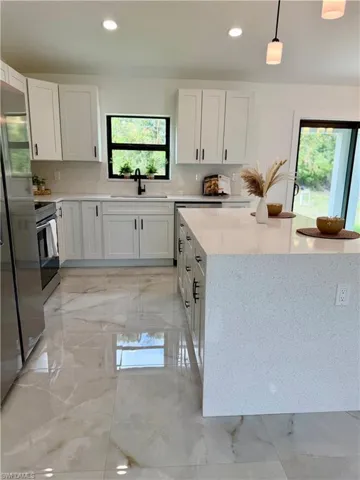 Modern kitchen featuring an expansive island with a light-toned countertop, white cabinetry with dark hardware, stainless steel appliances, and large format polished tile flooring