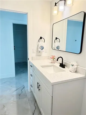 Contemporary bathroom vanity featuring white cabinetry, a speckled countertop, an undermount sink with a matte black faucet, and a rectangular mirror with a black frame