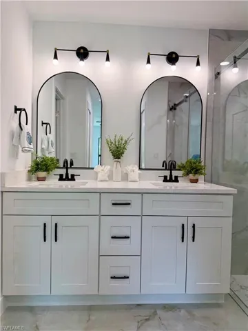 Dual vanity with white shaker cabinetry, matte black hardware, and two arched mirrors