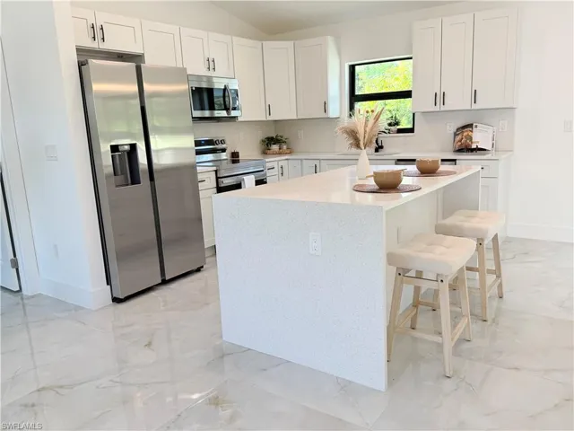 Modern kitchen featuring a central island with countertop seating, white shaker cabinetry, stainless steel appliances, and a tile backsplash