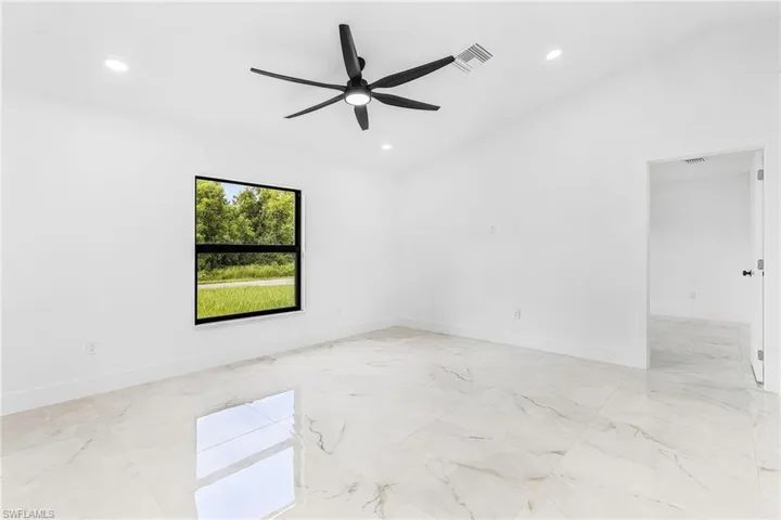 Spacious room featuring large format tile flooring, a black ceiling fan with integrated lighting, recessed ceiling lights, and a window overlooking natural green scenery