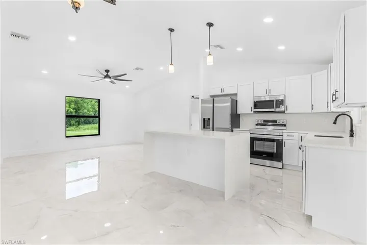 Spacious kitchen and living area featuring a large quartz island, stainless steel appliances, white cabinetry, and polished tile flooring