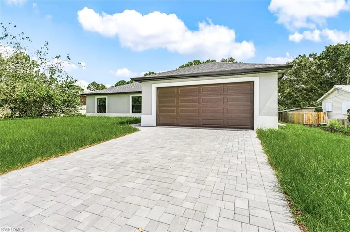 View of front facade featuring a front lawn, stucco siding, decorative driveway, and a garage