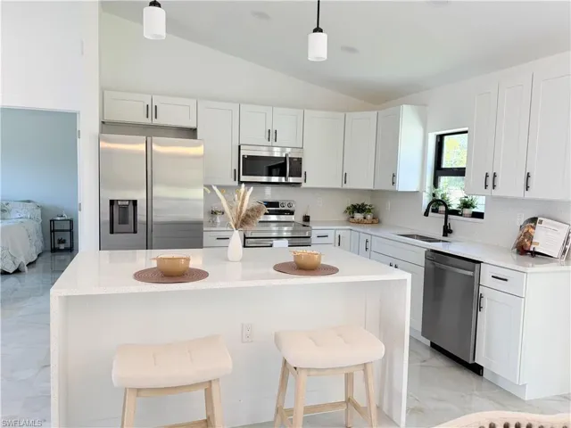 Kitchen featuring white cabinetry with dark hardware, stainless steel appliances, a white tile backsplash, and a large central island with a waterfall countertop