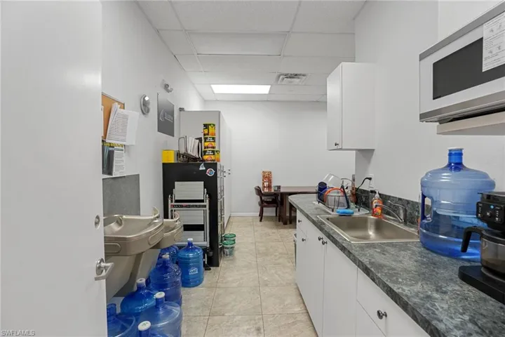 Kitchen with white microwave, a drop ceiling, white cabinetry, light tile patterned flooring, and dark countertops