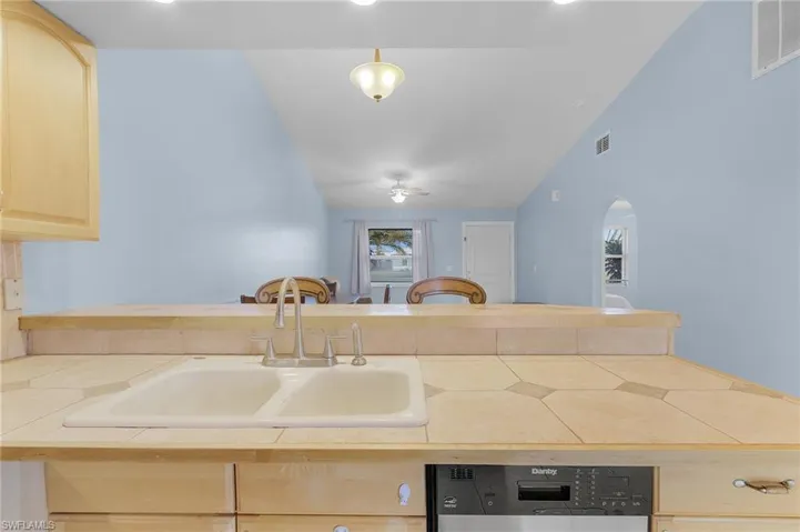 Kitchen featuring tile countertops, light wood finish cabinetry, dishwasher, a peninsula, and ceiling fan