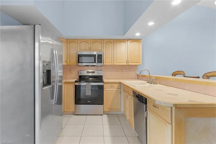 Kitchen featuring stainless steel appliances, light wood finish cabinets, decorative backsplash, light tile patterned flooring, and recessed lighting
