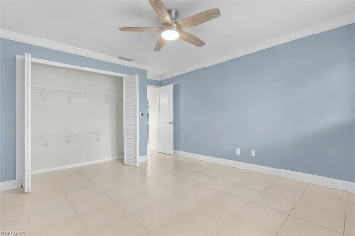 Unfurnished bedroom featuring ornamental molding, a ceiling fan, a closet, and light tile patterned flooring