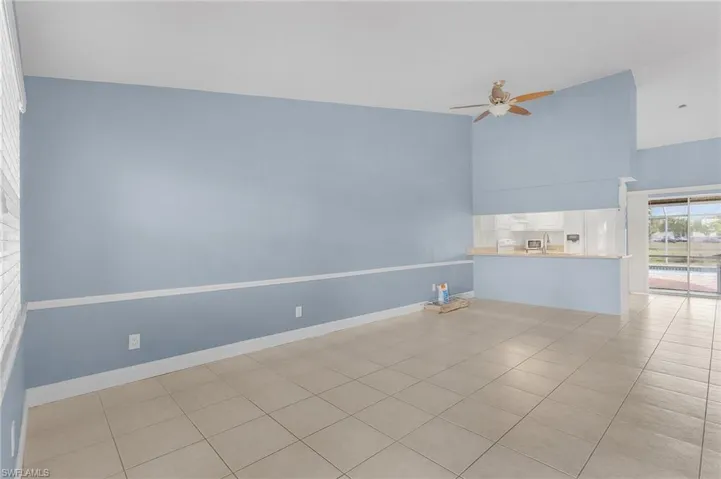 Empty room with ceiling fan, a high ceiling, and light tile patterned floors