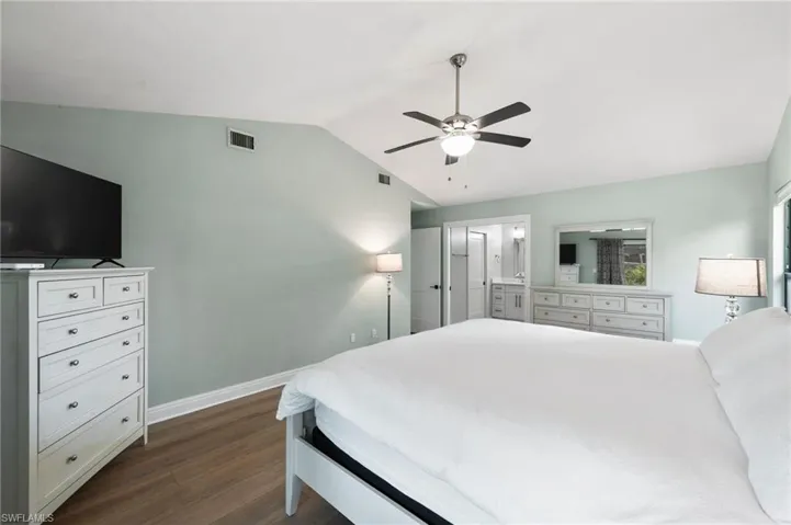 Bedroom with ensuite bath, ceiling fan, dark hardwood / wood-style flooring, and lofted ceiling