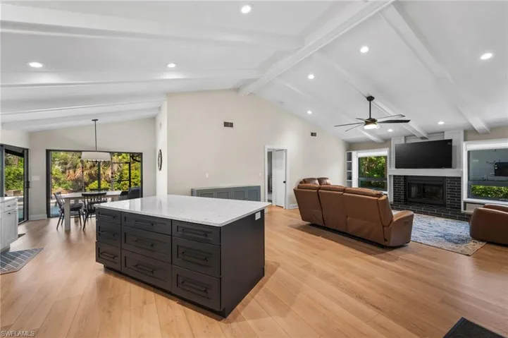Kitchen featuring vaulted ceiling with beams, light stone counters, light hardwood / wood-style flooring, plenty of natural light, and decorative light fixtures