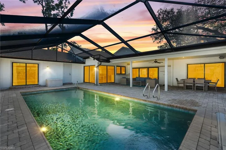Pool at dusk with an outdoor hangout area, glass enclosure, and a patio area