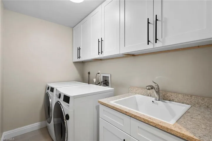 Laundry area featuring separate washer and dryer, sink, light tile patterned floors, and cabinets