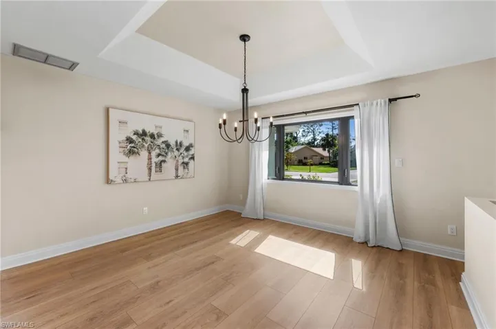 Unfurnished dining area featuring a chandelier, light wood-type flooring, and a raised ceiling