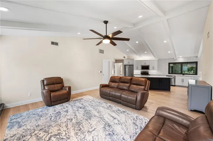 Living room with lofted ceiling with beams, light hardwood / wood-style floors, ceiling fan, and sink