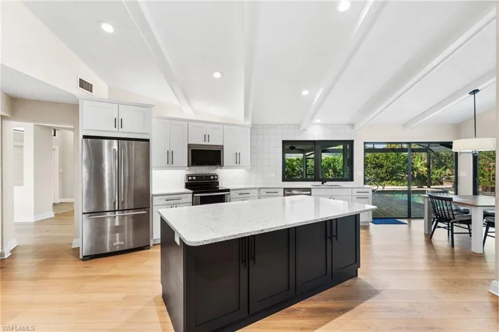 Kitchen with white cabinets, lofted ceiling with beams, light wood-type flooring, and appliances with stainless steel finishes