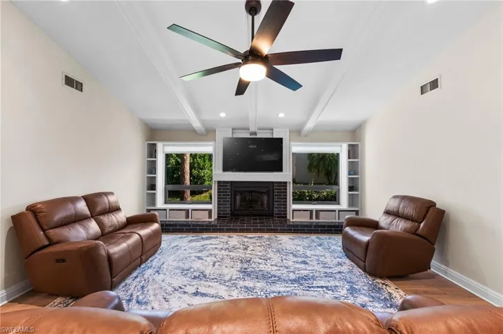 Living room with a fireplace, vaulted ceiling with beams, light hardwood / wood-style floors, and ceiling fan