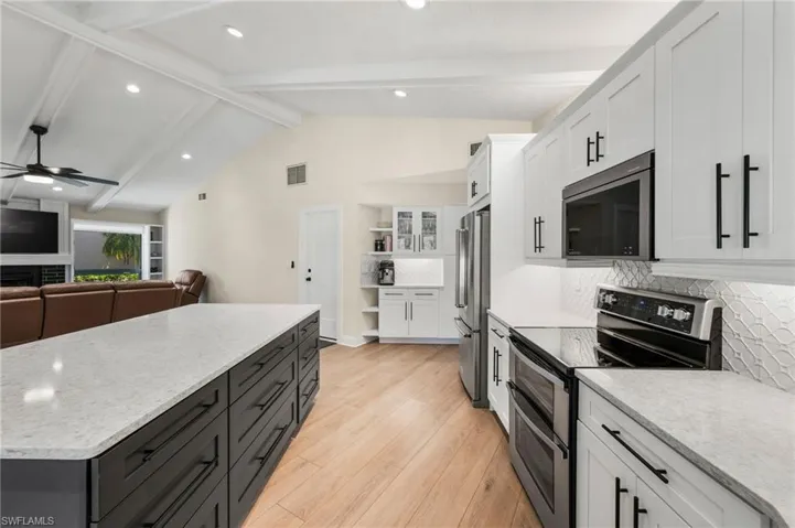 Kitchen featuring backsplash, lofted ceiling with beams, light wood-type flooring, white cabinetry, and stainless steel appliances