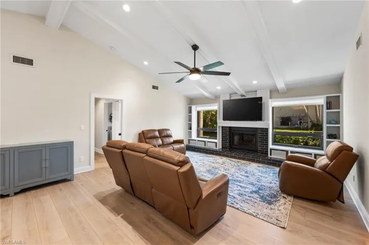 Living room featuring high vaulted ceiling, ceiling fan, light wood-type flooring, a fireplace, and beam ceiling