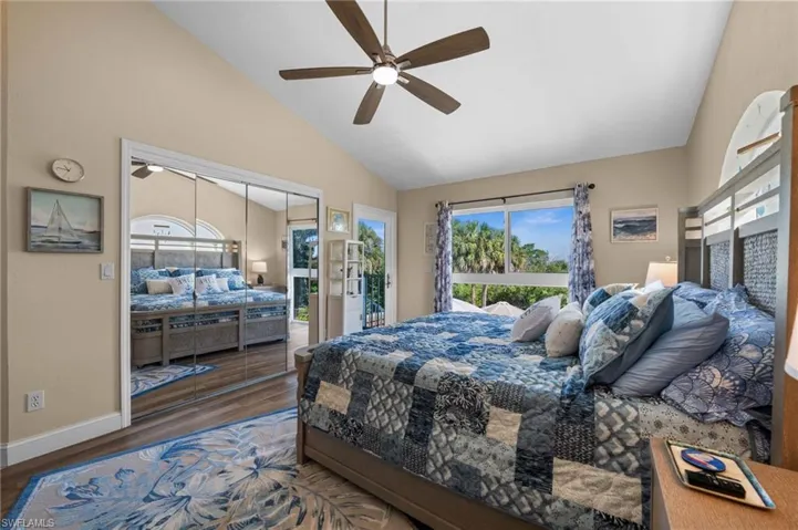 Bedroom featuring access to exterior, a closet, wood finished floors, multiple windows, and high vaulted ceiling